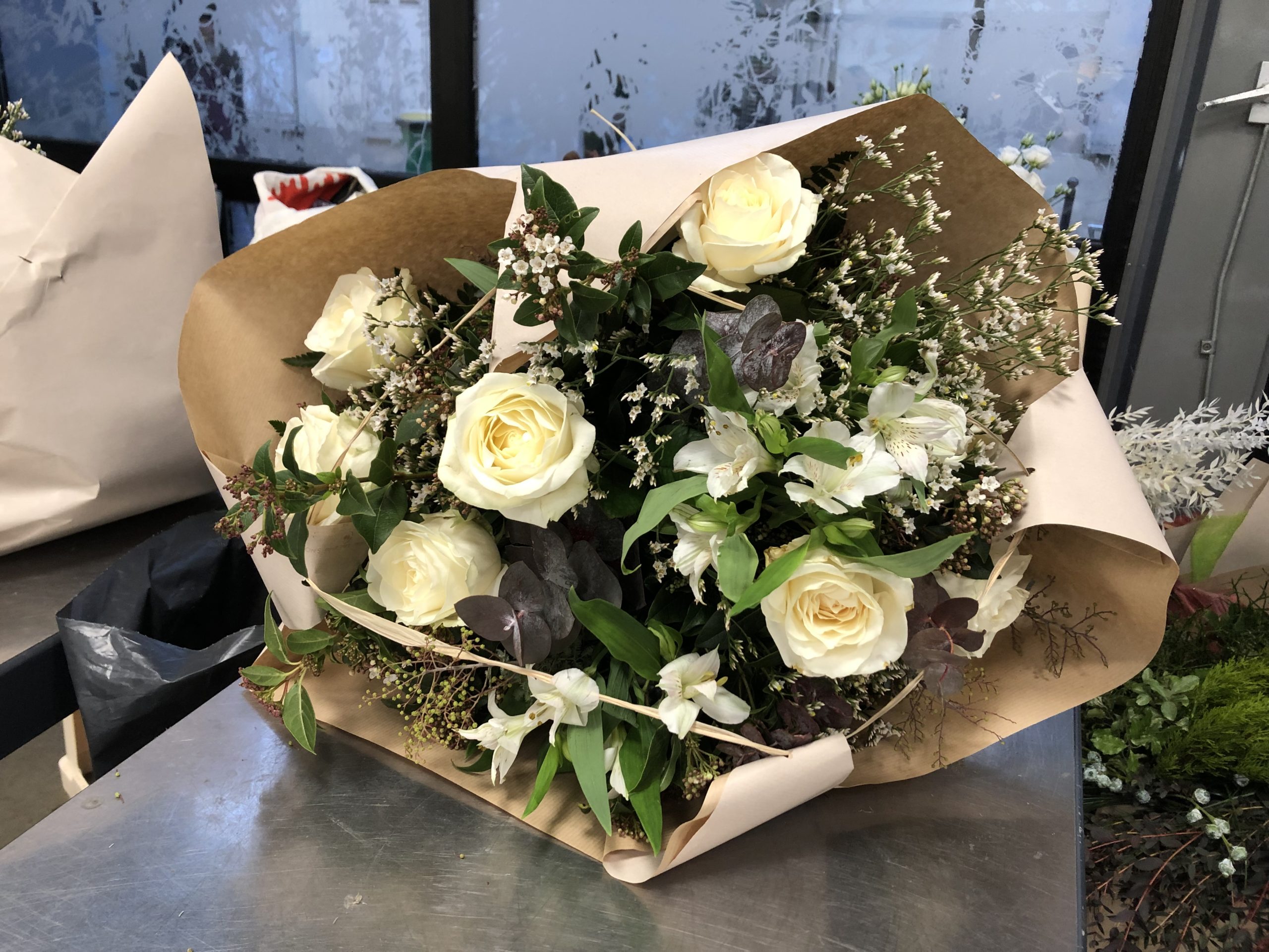Bouquet rond décoratif, emballé (roses blanches avalanche, limonium, eucalyptus, laurier tin, mimosa gris, alstromeria, fougères US)